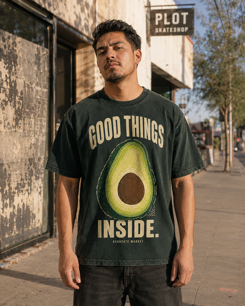 Peel green heavyweight tee worn on the street outside a skate shop, front print visible.