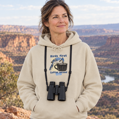 Woman in a desert canyon wearing the sand Birds First, Coffee Second hoodie with binoculars