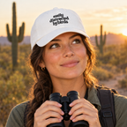 Woman on a desert trail wearing the white Easily Distracted by Birds dad cap, holding binoculars